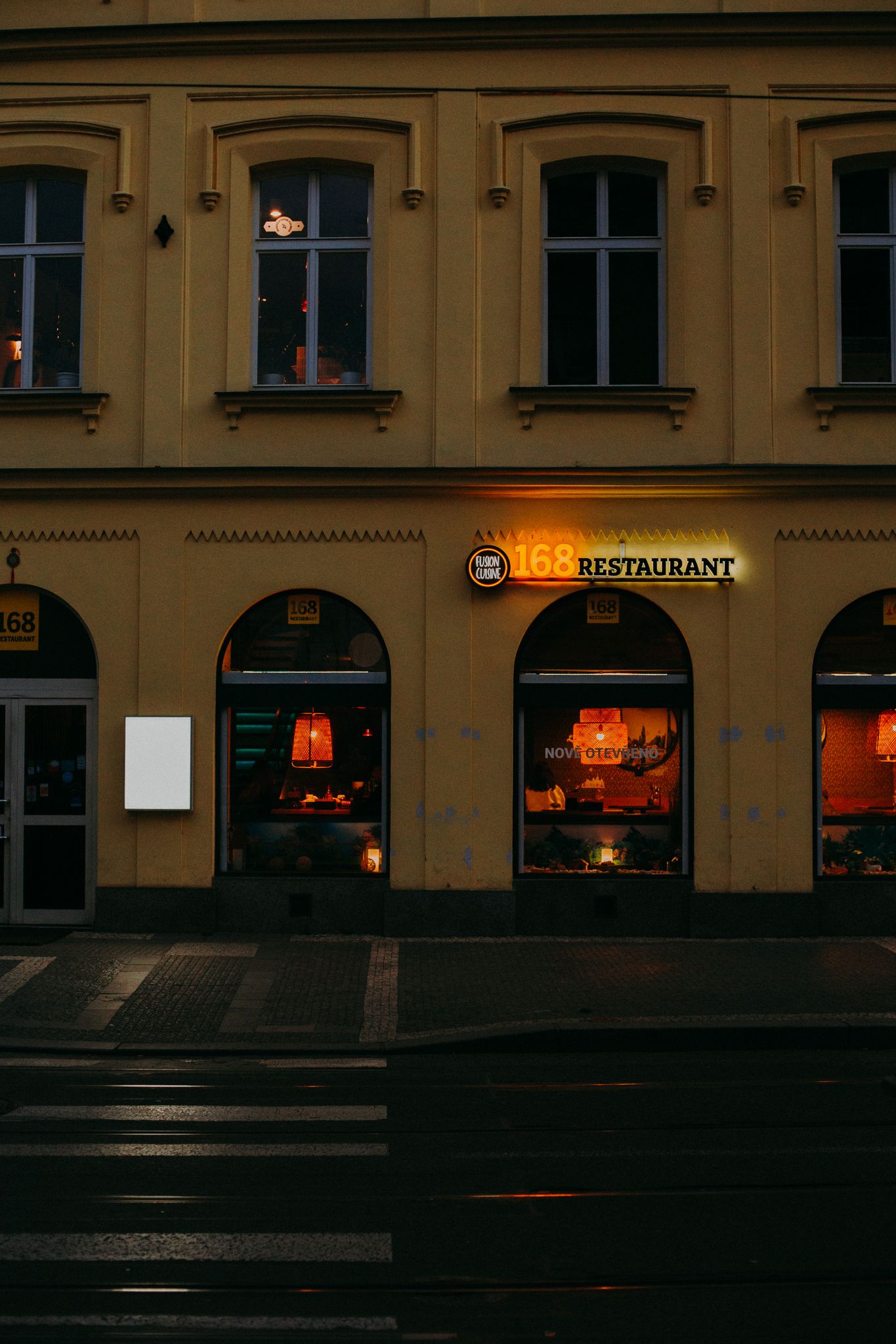 Illuminated restaurant facade in Prague with reflections on wet street at night.