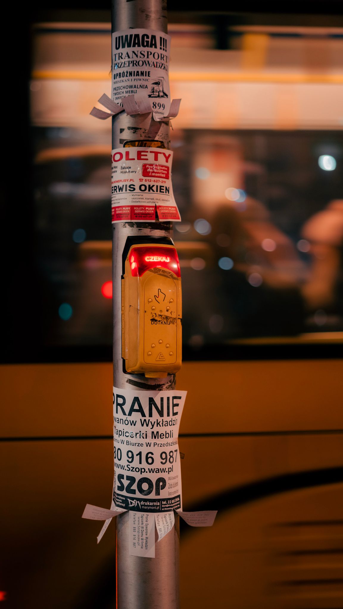View of a street pole covered with flyers and signs in a bustling city at night.